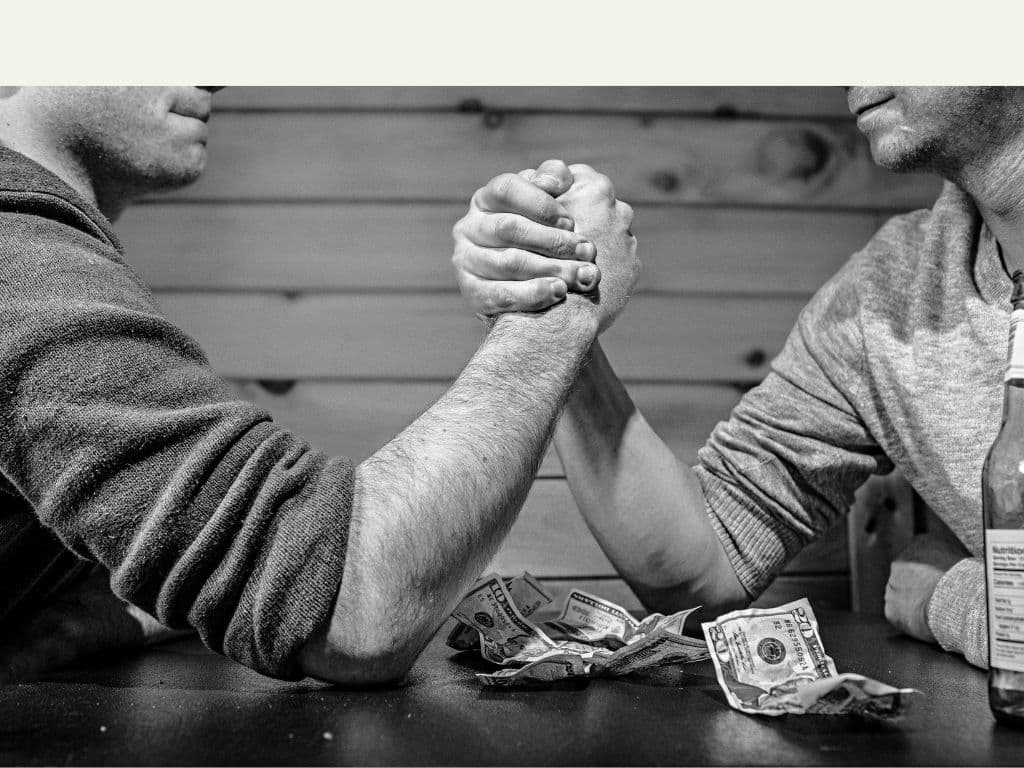 Two men having an arm wrestle in a monochrome photo with money on the table and a drink off to the right
