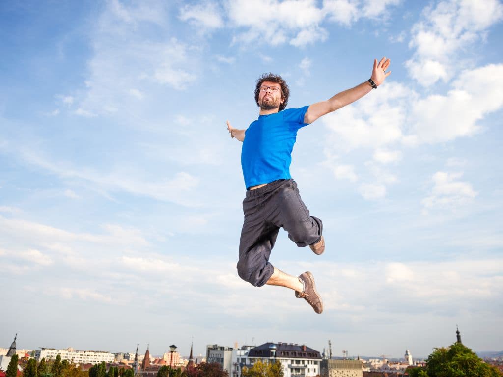 A man jumping in the sky while wearing a blue t shirt in the daytime