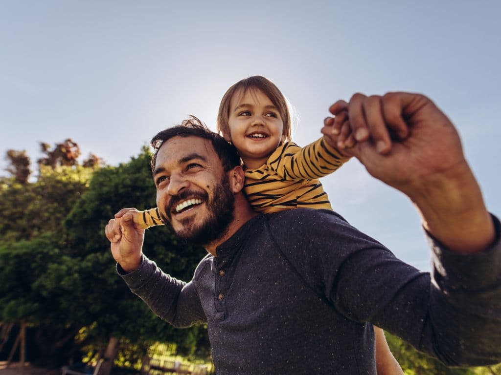 A young father and his child riding upon his back in broad daylight