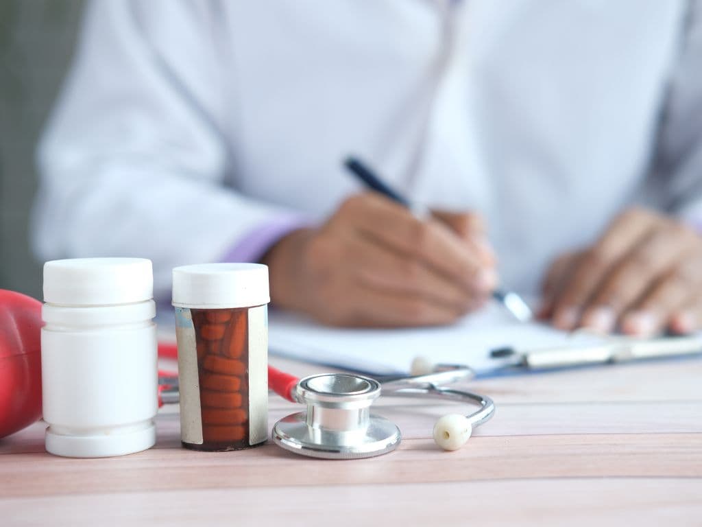 A doctor writing on a piece of paper while some pills are in front of him