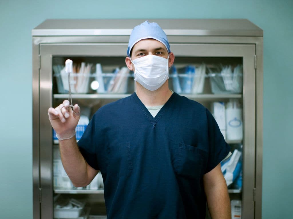 A doctor posing in front of a bookshelf while wearing a mask